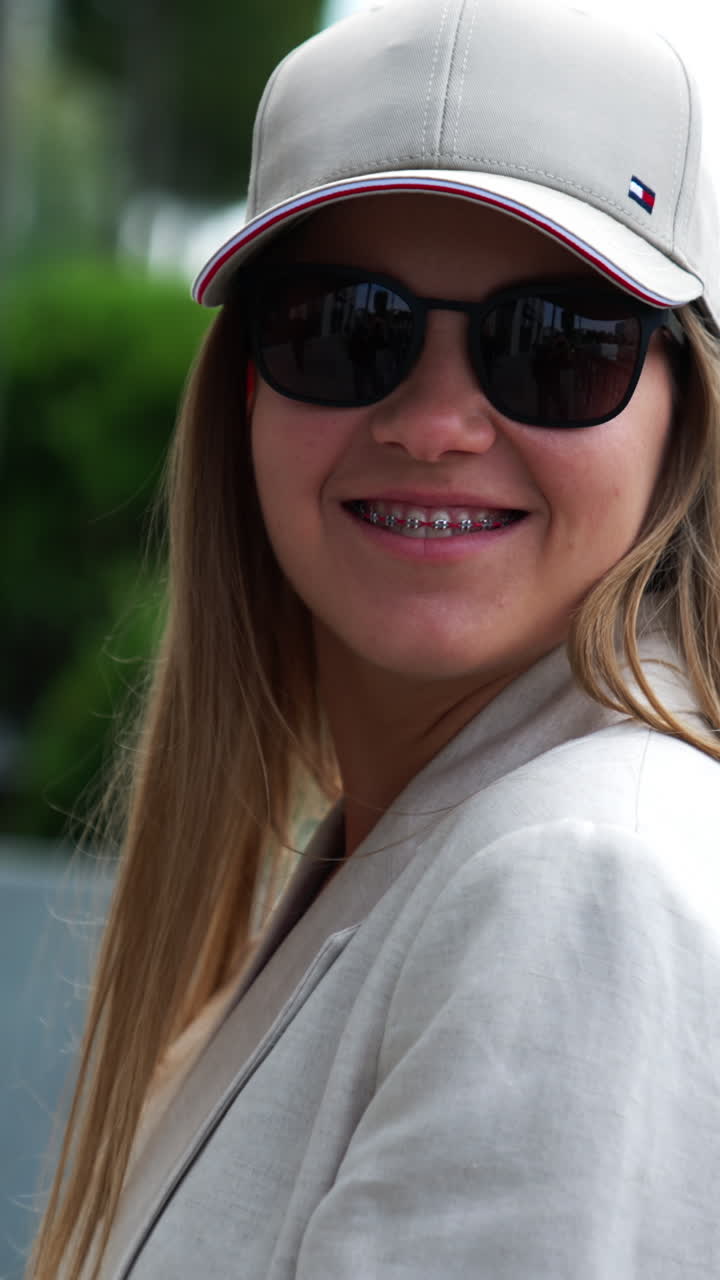 Smiling happy woman in black sunglasses and cap outdoors. Stylish fashionable young lady in the urban surrounding. Close up portrait. Vertical video