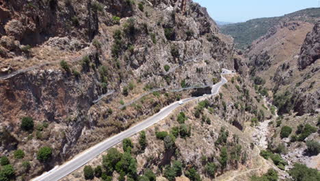 Vista-Aérea-De-Los-Coches-Que-Circulan-Por-Una-Peligrosa-Carretera-Estrecha-Entre-El-Cañón-Rocoso-Durante-El-Día