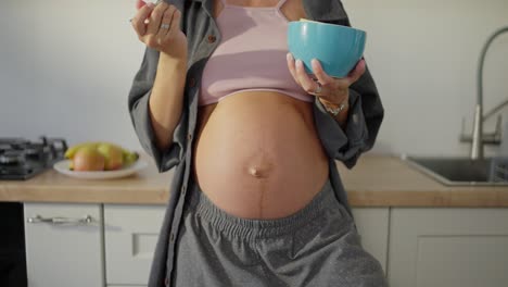 close-up of a pregnant woman eating fruit salad from a blue bowl in the kitchen in the morning during breakfast