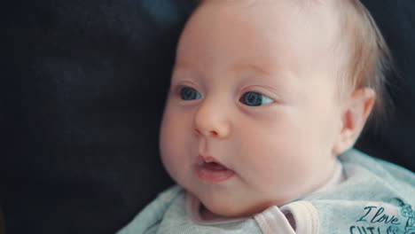 a beautiful blue-eyed newborn baby lying on a black background and looking away