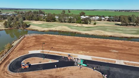 vista aérea de la máquina de pavimentación de construcción de carreteras y rodillos con campo de golf más allá