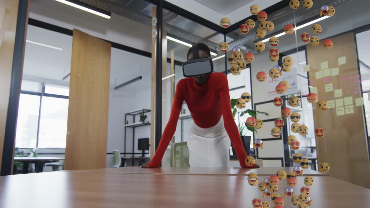 woman using VR headset leaning on conference table, displaying floating emoji icons in tech office