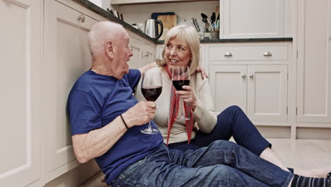 elderly couple toasting wine glasses in kitchen