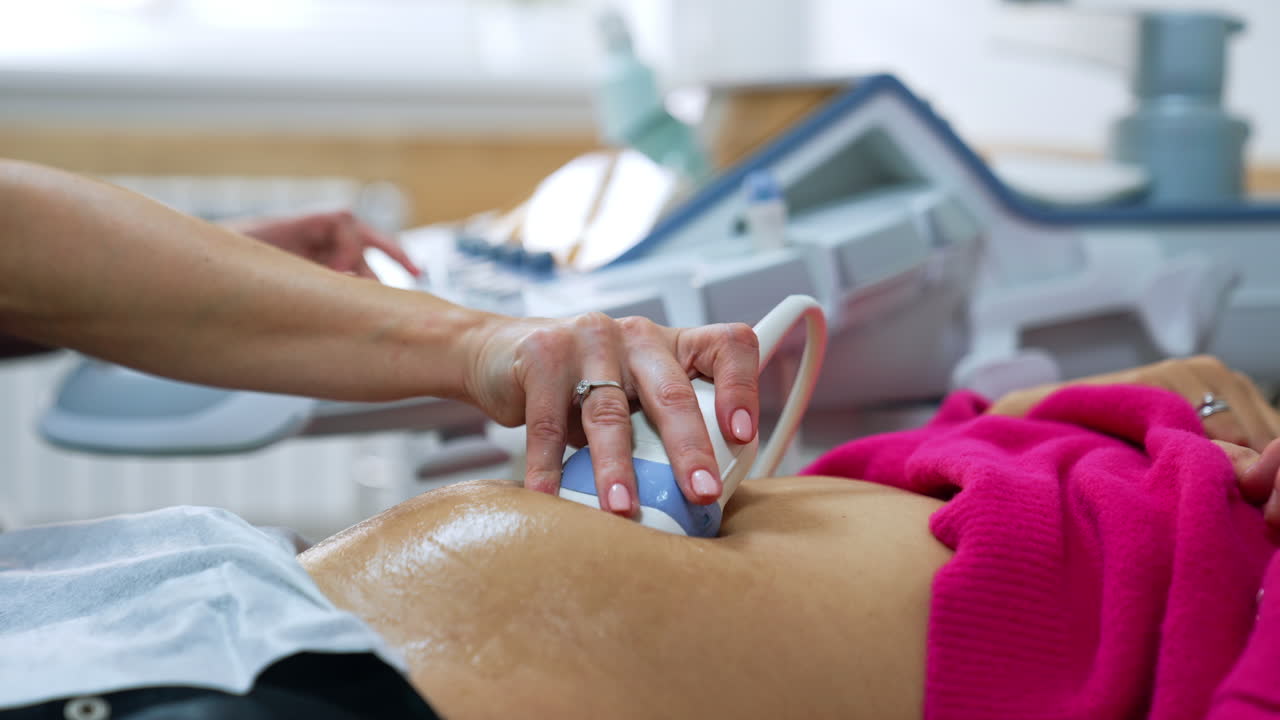 Female doctor's hand moving the ultrasound device by the patient's belly. Ultrasonic pregnancy scanning.