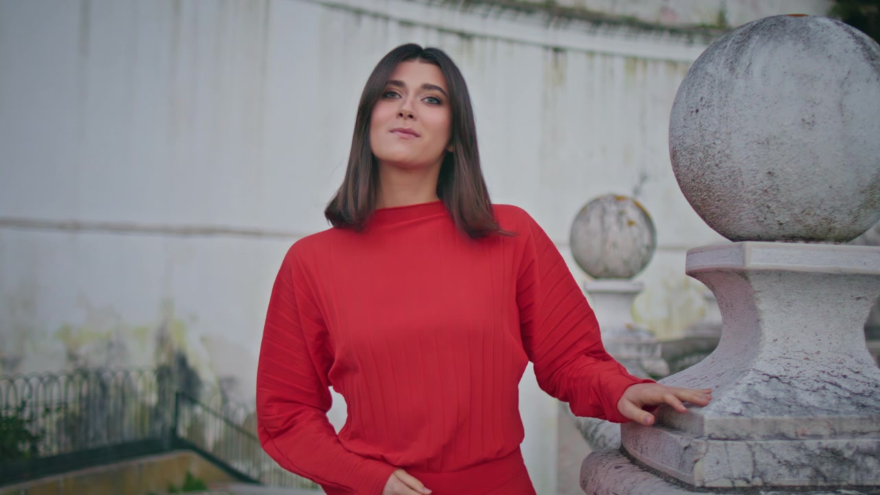Wanita elegan berbaju merah bersandar pada balustrade batu. Gadis berpose di teras kota tua