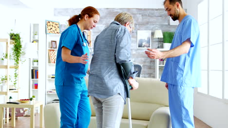 médico masculino y su asistente en un hogar de ancianos ayudando a una mujer anciana que camina con muletas