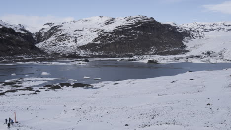 Rotating-aerial-shot-of-a-frozen-lake-surrounded-by-Icelandic-snow-covered-mountains