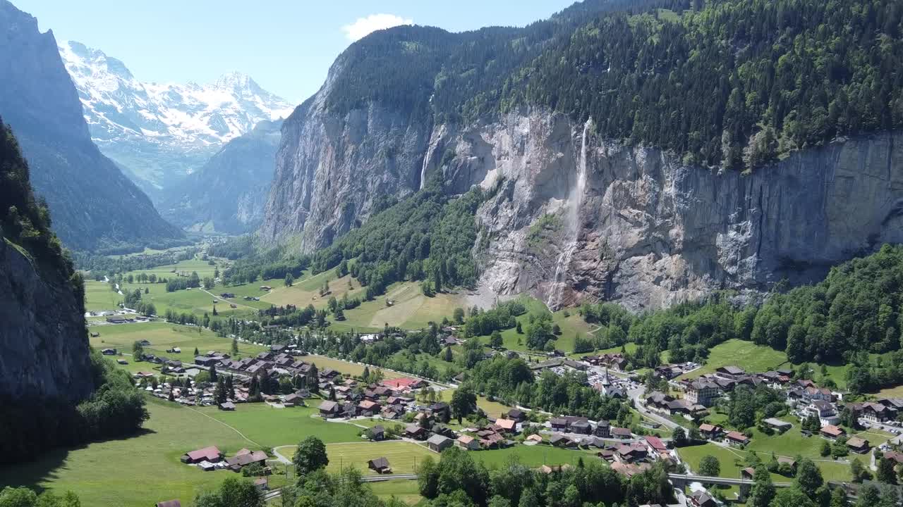 Drone flight through the green valley of Lauterbrunnen with a view of the beautiful waterfall and the snow-covered Swiss Alps in the background