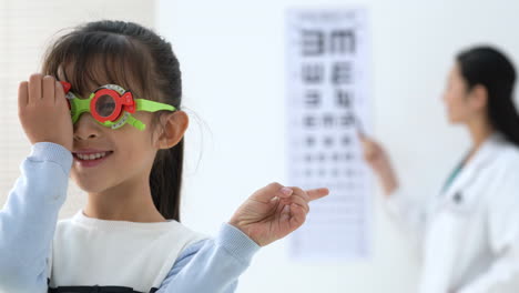 female optometrist ophthalmologist testing eyesight of little girl with eyeglasses indoors clinic