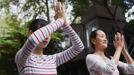 Happy-asian-mother-exercising-in-garden-with-daughter,-practicing-tai-chi-together