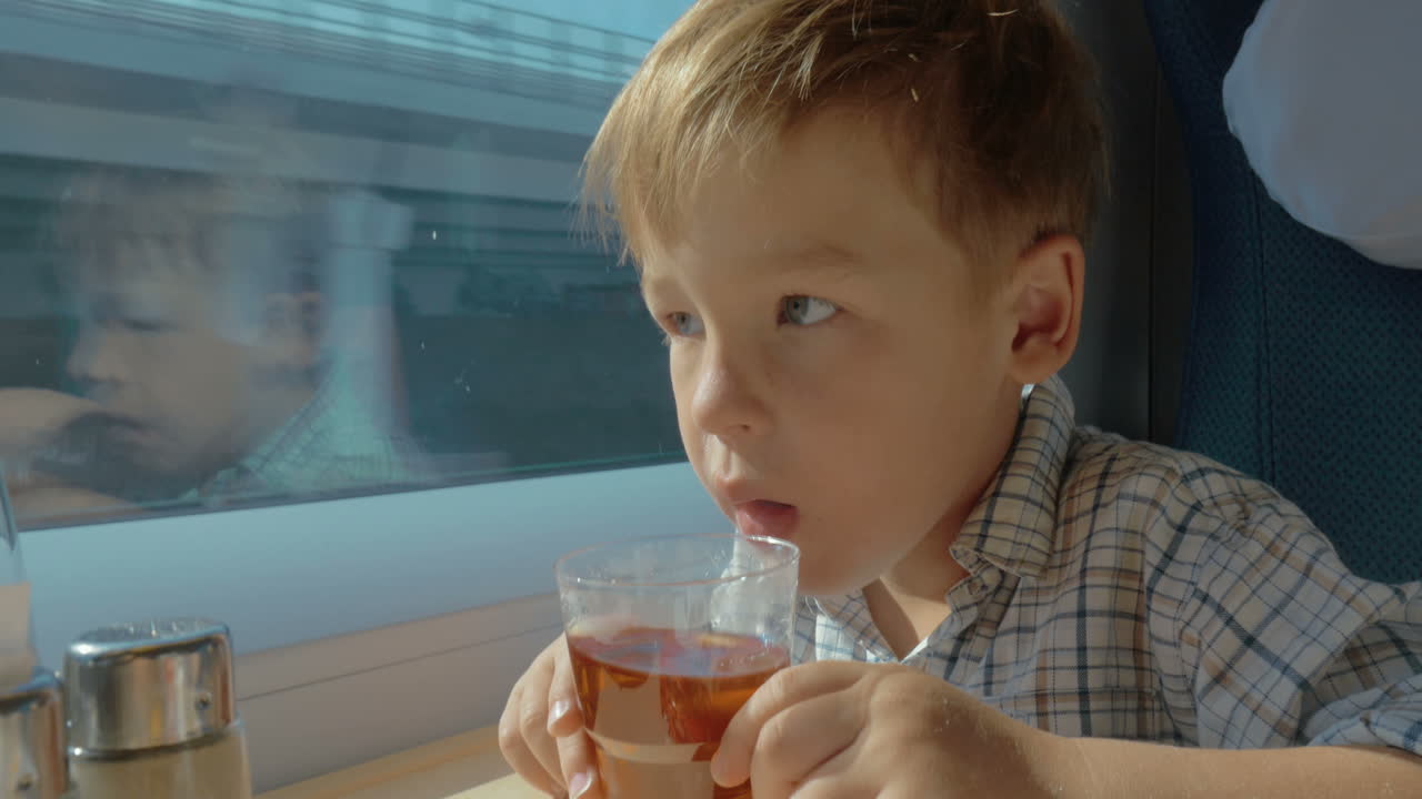 niño tomando té y mirando por la ventana en un tren en movimiento