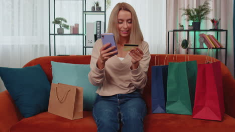 feliz mujer joven adicta a las compras sentada con bolsas de compras haciendo pagos en línea con tarjeta de crédito