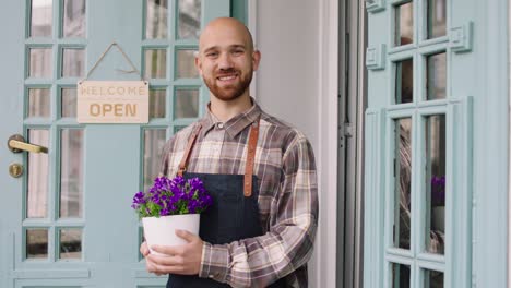 concept of small business florist entrepreneur the charismatic man owner of the floral shop smiling large to the camera and holding a flowers pot in hands