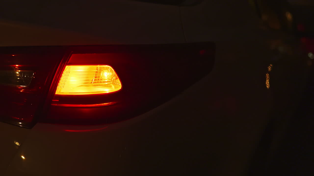 Escena nocturna mostrando la luz trasera de un coche aparcado en una calle de la ciudad, con otras luces de vehículos al fondo durante el crepúsculo