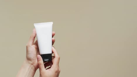 hands of woman with tube of cream on beige background with copy space, slow motion