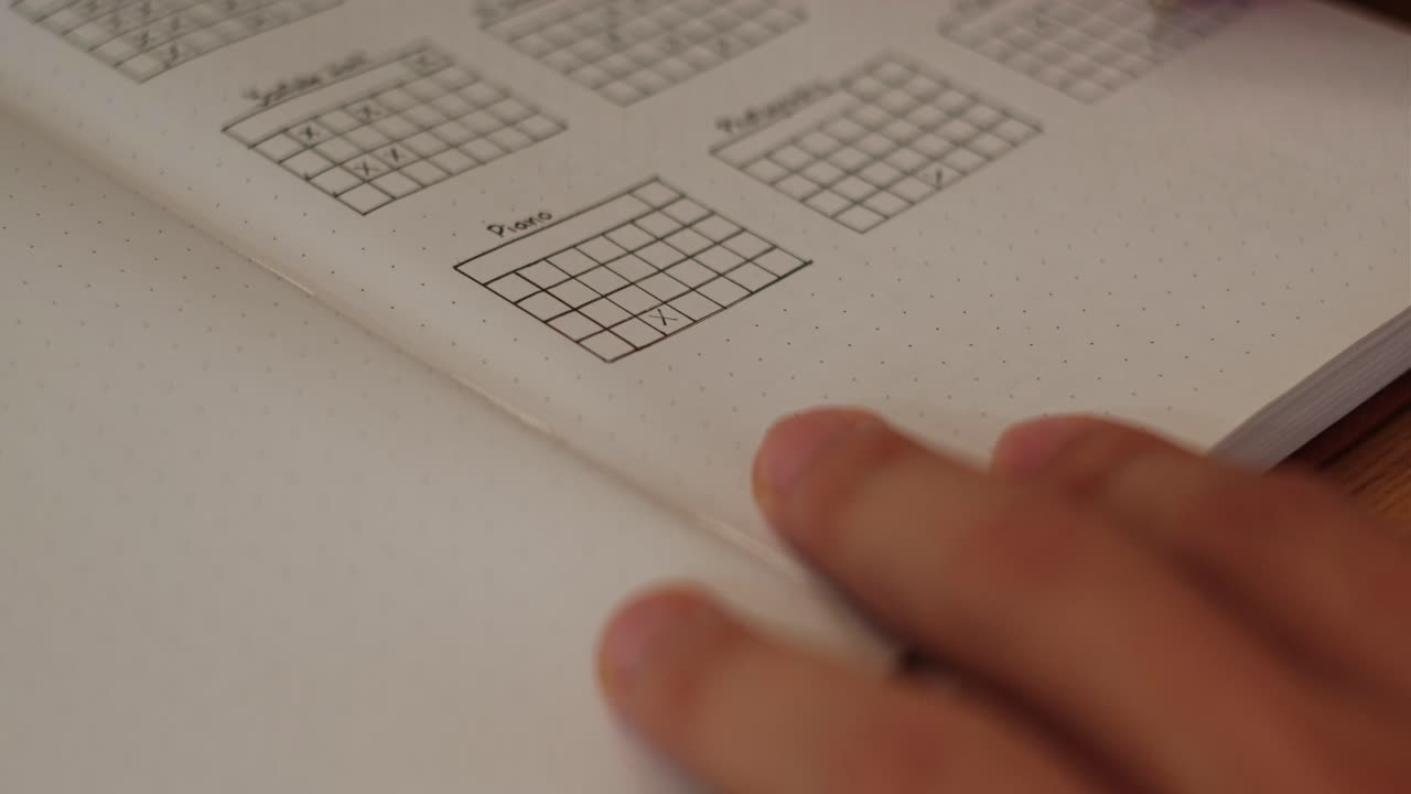 Close-up static shot of a hand and pen filling out habit tracker grid inside journal spreadsheet