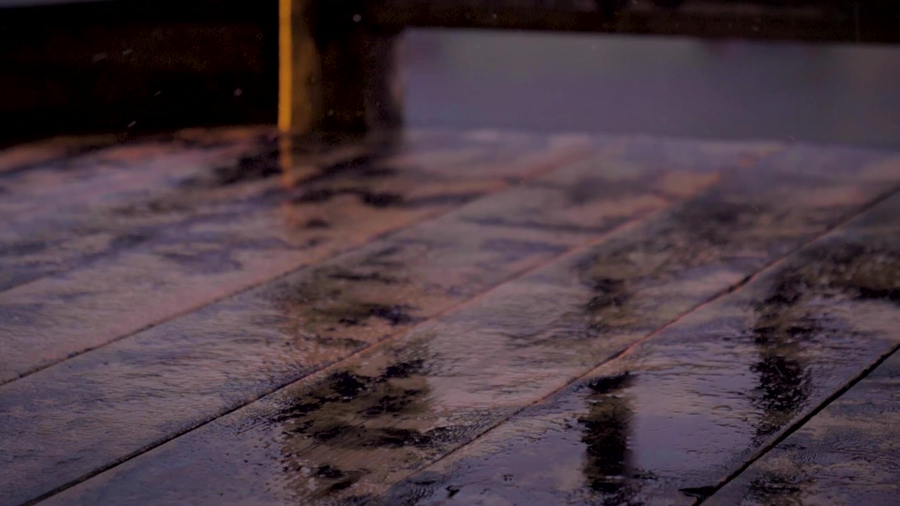 Vand drypper på et trædæk og sprøjter. Regnfuld udendørsscene. Slowmotion