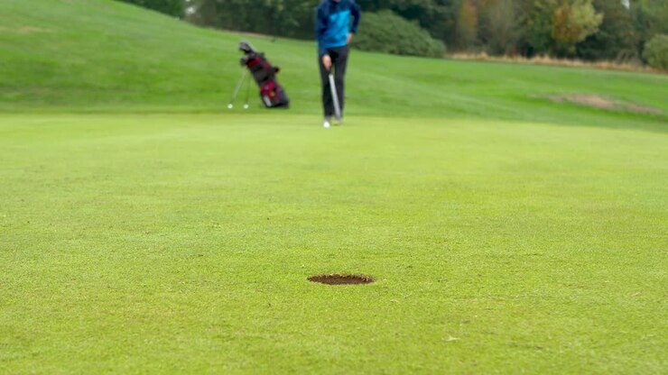 Golfista sfocato che si prepara per un putt di media distanza con la messa a fuoco sulla buca.