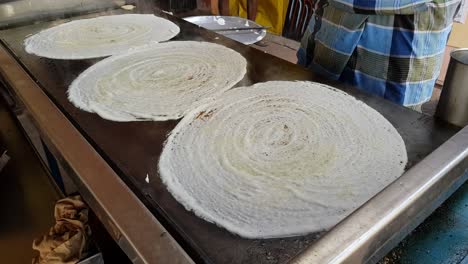 un hombre haciendo dosa en un enorme plato de piedra