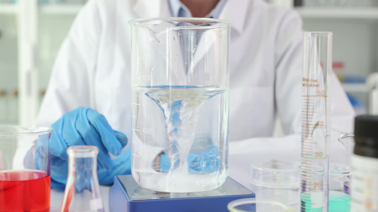 A close-up of a scientist stirring a liquid in a beaker with a magnetic stirrer in a laboratory