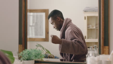 happy african american man dancing in bathroom looking in mirror having fun morning routine getting ready enjoying positive self image wearing bathrobe