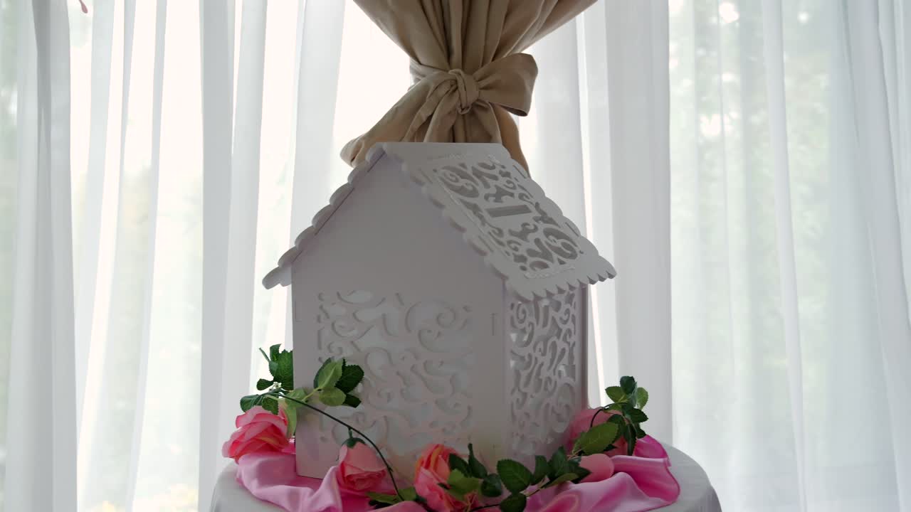 Handheld close-up of ornate white card box with pink roses and draped fabric