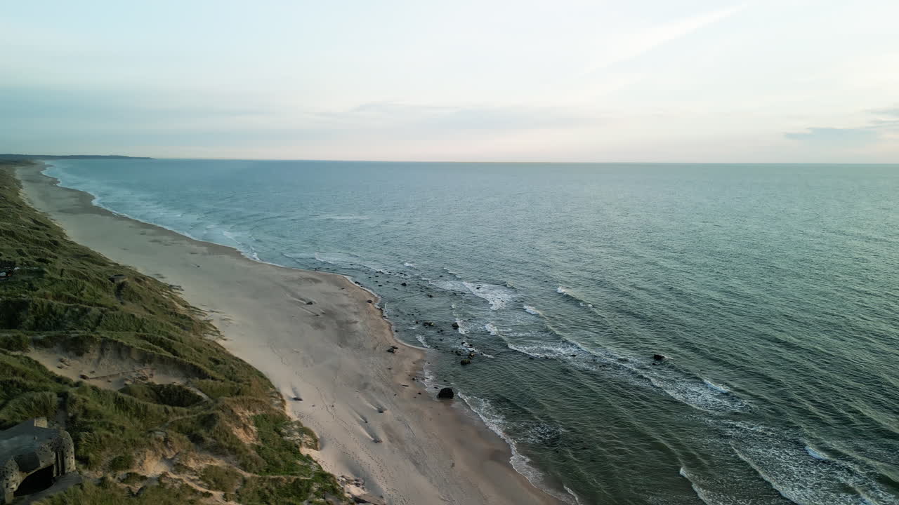 Evening drone flight with upward pan over the empty beach on the North Sea in Denmark. The sunset casts long shadows on the waves and dunes