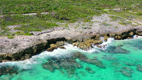 overhead aerial of turquoise blue waves crashing onto sharp rocks on cozumel island in mexico