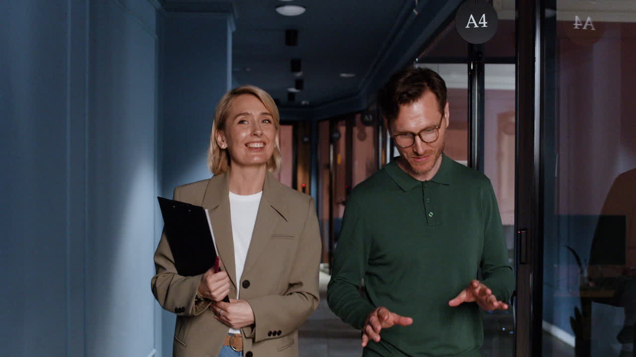 Two business colleagues walking and discussing in a modern office hallway