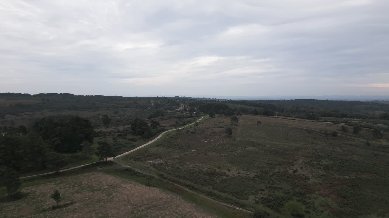 Gravel road, green meadow and moody sky, aerial view