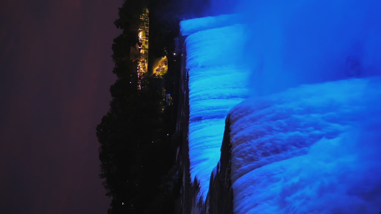 Vertical 4k Video - Night View Of Niagara Falls Water Streams Lit By A Blue Floodlight 4k Video