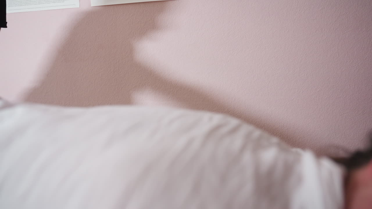 Soft shadow of massage therapist reflected on pink wall during massage session, with blurred foreground showing client covered in white sheet, creating calm atmosphere