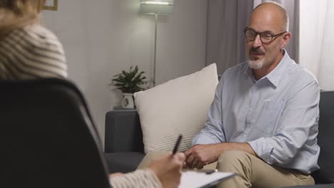 mature man sitting on sofa talking with female counsellor about general or mental health issue 2