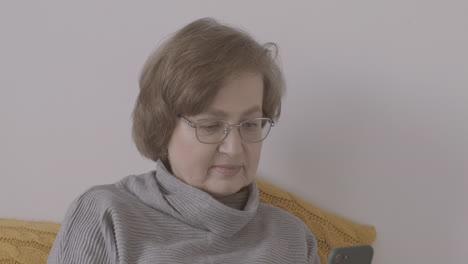 Senior-Woman-With-Eyeglasses-Sitting-On-Bed-Using-Smartphone-1