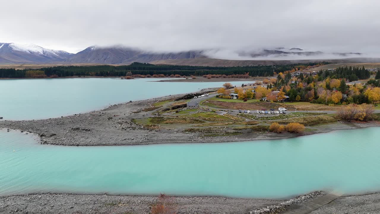 Aerial footage captures Lake Tekapo's turquoise waters and autumn foliage under overcast skies, showcasing the serene landscape of Canterbury, New Zealand