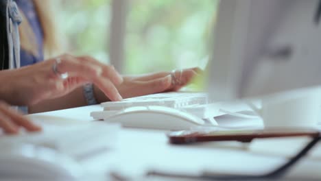 una foto de cerca de una mujer de negocios escribiendo a mano y trabajando en la computadora en el escritorio.