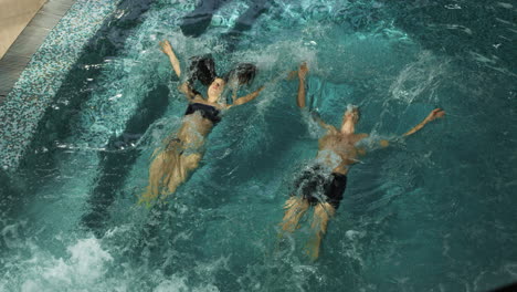 Couple-jumping-synchronously-in-pool.-Man-and-woman-submerging-under-water.