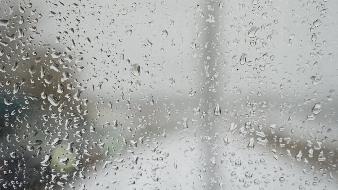 Rainy windshield shows distant lights. Rainsoaked windshield creates blurred scenery with distant bright spots. This scene captures rainy car journey with blurry road and shining distant lights