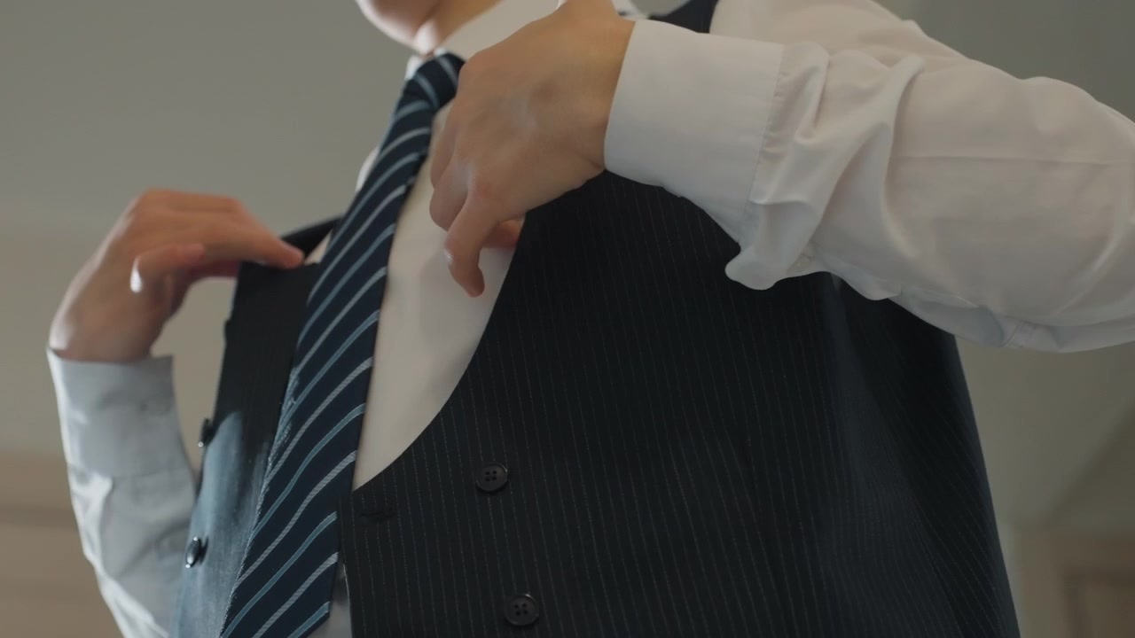 Hombre abotonándose el chaleco y ajustándose la corbata antes de partir, ángulos medios y primeros planos capturan las manos asegurando botones, colocando los tirantes y enderezando la corbata a rayas, los ángulos de cámara bajos enfatizan