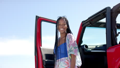 young african american woman stands by a red car outdoors on a road trip