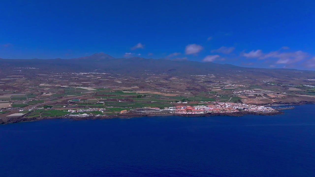 Vista aérea de un pueblo costero y tierras de cultivo junto al océano azul bajo un cielo despejado, Tenerife