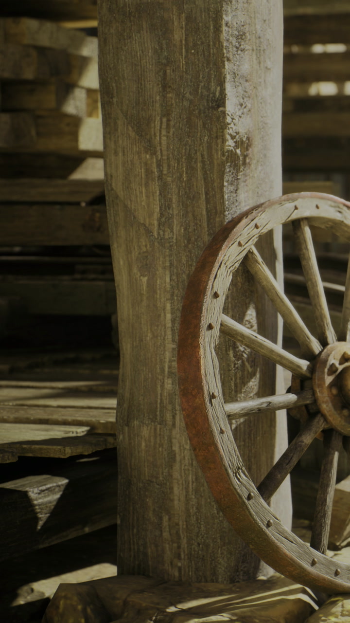Old wooden wheel rests against a weathered post in a rustic barn setting
