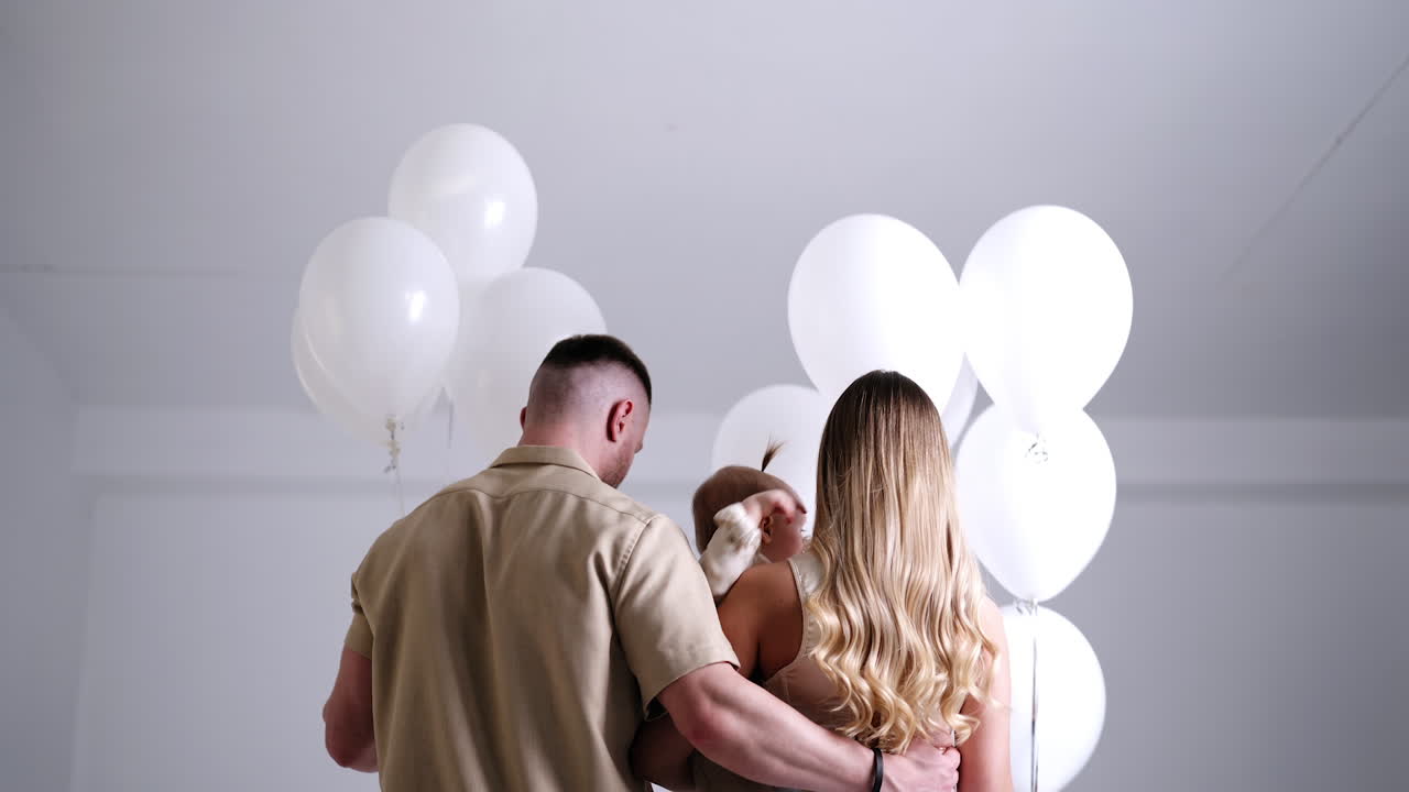Rear view of young parents with little baby. Studio footage of a family holding balloons. Low angle view.