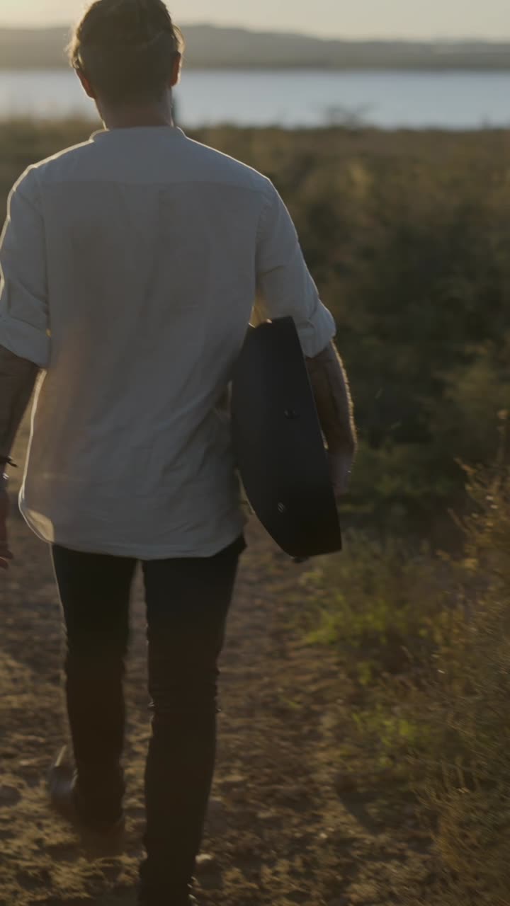 Man walking with a guitar at sunset
