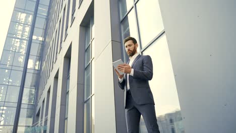 stylish bearded businessman in formal business suit standing working with tablet in hands