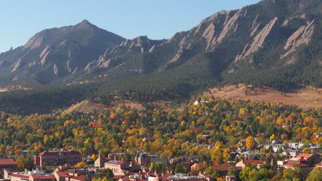 aerial up close view of flatiron mountains in boulder colorado surrounded by peak fall colors of green, red, and yellow trees showing the town and cu boulder campus