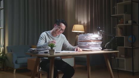 un hombre asiático sonriente disfruta trabajando con documentos en casa.