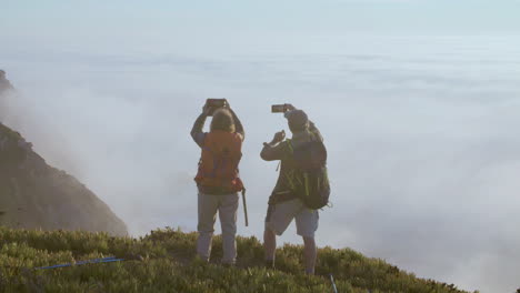 pareja mayor parada en la cima de la colina y tomando fotos por teléfono