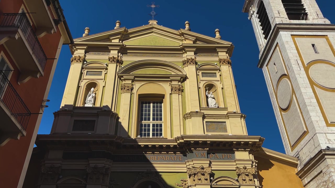 Vista dal basso della facciata barocca ornata e del campanile della Cattedrale di Sainte-Réparate a Nizza, Francia, che risplende alla luce del sole sotto un cielo blu intenso