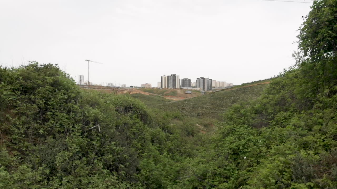 cámara caminando entre las verdes colinas en dirección a nuevos edificios residenciales en el horizonte